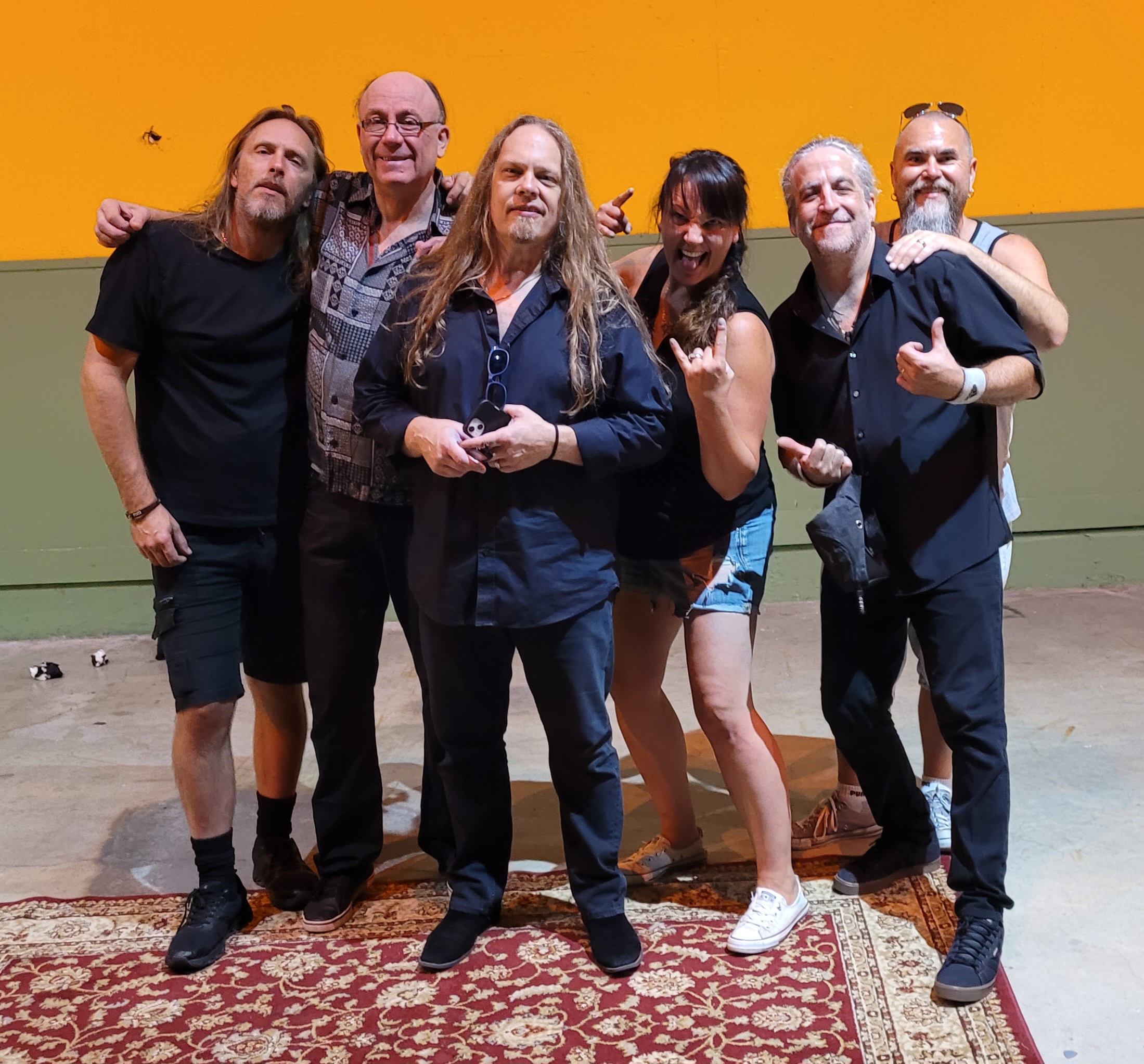 The Eagle Eyes band and crew posing together on a Persian rug on an outdoor community stage